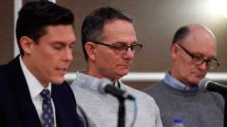 Tad Deluca, center, listens as attorney Parker Stinar addresses the media during a news conference, Thursday, Feb. 27, 2020 in Southfield, Mich. Deluca, a University of Michigan wrestler from the 1970s, says he was kicked off the team and lost his financial aid after complaining to a coach that he had been abused by a sports doctor. Deluca identified himself as the whistleblower whose 2018 complaint about the late Dr. Robert E. Anderson led to a police investigation. (AP Photo/Carlos Osorio)