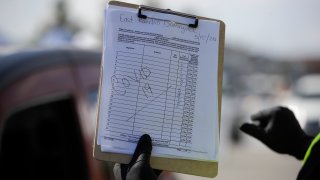 Volunteer Dijon Barnes holds a sign which reads "COVID-19" at a food distribution center Friday, May 15, 2020, in Compton, Calif. Unemployment figures continue to rise and more Americans are relying on food handouts amid the coronavirus pandemic.