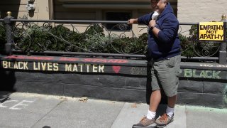James Juanillo poses next to chalk written outside of his home in San Francisco, Sunday, June 14, 2020. The CEO of a cosmetic company issued an apology Sunday after she and her husband confronted Juanillo and threatened to call police because he stenciled "Black Lives Matter" in chalk on his San Francisco property, as the couple asserted that they know Juanillo doesn’t live there and is therefore breaking the law.