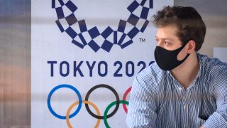 Un hombre con una mascarilla se sienta en una parada de autobús frente a un anuncio de los Juegos Olímpicos de Tokio 2020 en Bangkok este 16 de marzo de 2020.