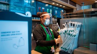 In this May 12, 2020, file photo, a Starbucks employee wears a face shield and mask as she makes a coffee in Ronald Reagan Washington National Airport in Arlington, Virginia.