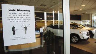 A sign advising customers to practice social distancing is displayed on the door of a General Motors Co. Buick and GMC car dealership