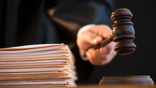 A hand holds a gavel next to a stack of manila folders.