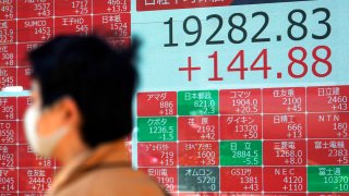 In this April 23, 2020, file photo, a man wearing a mask against the spread of the new coronavirus walks past an electronic stock board showing Japan's Nikkei 225 index at a securities firm in Tokyo.