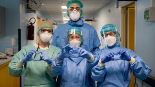 Nurses in Italy dressed in surgical gowns, gloves and protective gear making heart signs to the camera