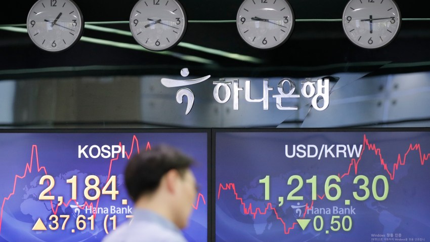 A currency trader walks by the screens showing the Korea Composite Stock Price Index (KOSPI), left, and the foreign exchange rate between U.S. dollar and South Korean won at the foreign exchange dealing room in Seoul, South Korea, Thursday, June 4, 2020.