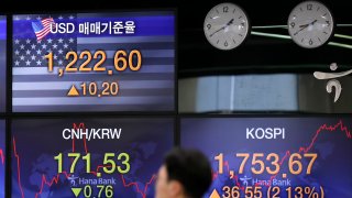 In this March 31, 2020, file photo, a currency trader walks by the screens showing the Korea Composite Stock Price Index (KOSPI), right, and the foreign exchange rate between U.S. dollar and South Korean won, left top, at the foreign exchange dealing room in Seoul, South Korea.