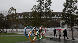 In this March 4, 2020, file photo, people walk past the Olympic rings near the New National Stadium in Tokyo.