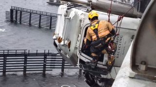 In this Monday, April 13, 2020, photo provided by the Chesapeake Fire Department, a Chesapeake firefighter tries to rescue the driver of a tractor trailer on the High Rise Bridge over the Elizabeth River, in Chesapeake, Va.