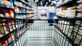 Personal perspective of a shopper pushing shopping trolley along product aisle while shopping in a supermarket