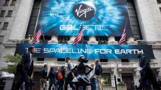 Pedestrians pass in front of a banner displaying Virgin Galactic Holdings Inc. signage during the company's initial public offering (IPO) outside the New York Stock Exchange (NYSE) in New York, U.S., on Monday, Oct. 28, 2019.