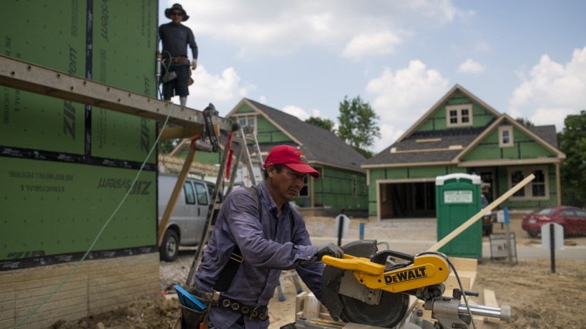 A worker cuts a piece of wood trim to size outside a home under construction