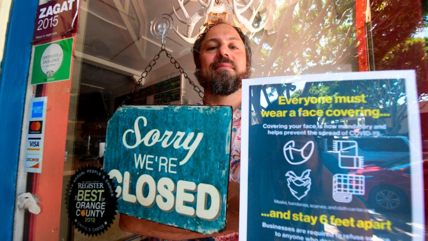 In this July 28, 2020, file photo, Gabriel Gordon stands behind the glass entrance door to his restaurant Beachwood BBQ, open for 14 years in Seal Beach, California, but closing soon due to the economic situation around the coronavirus pandemic.
