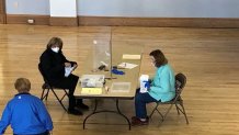 workers sit divided by plexiglass, counting absentee ballots