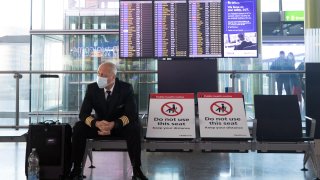 A member of flight crew sits next to social distancing signs in the check-in area in at London Heathrow Airport Ltd. in London, U.K., on Saturday, Dec. 19, 2020.