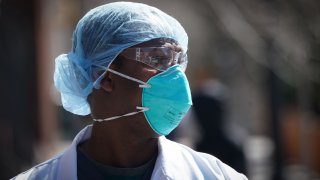 A healthcare worker wears a N95 respirator with two straps that fit around the head.