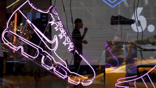 Seen through a store window, a Nike employee stands in the entryway of the Nike SoHo store in New York City.