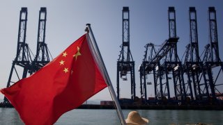 A Chinese flag attached to the back of a boat flaps in the wind as cargo containers sit on the dock of Shenzhen Port in Shenzhen, China.