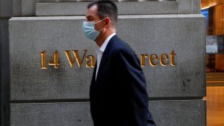 A man wearing a protective face mask walks by 14 Wall Street in the financial district of New York, November 19, 2020.
