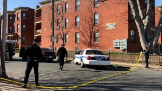 Police tape blocks off a crime scene. A police cruiser and brick building are scene in the background.