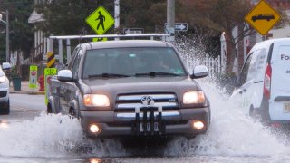 This Oct. 11, 2019 photo shows a car kicking up spray while driving through a flooded street in Bay Head, New Jersey. With the highest tides of the year expected to arrive in New Jersey during the week of May 24, 2021, the state is launching a campaign to have residents document tidal flooding in their neighborhood and upload photos to a web site.