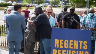 Jon Vaughn (R), former University of Michigan and former NFL football player, and Richard Goldman, a former UM student sports announcer, hug at a press conference on the University of Michigan campus on June 16, 2021 in Ann Arbor, Michigan.