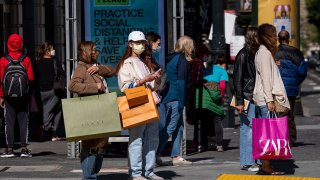 People wearing protective masks carry shopping bags while waiting to cross Geary Street in San Francisco