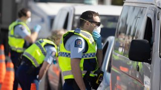 Police officers wearing protective masks talk to motorists at a checkpoint in the Bombay area of Auckland, New Zealand, on Wednesday, Aug. 12, 2020.