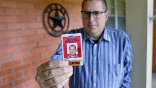Lance Lowry, a recently retired corrections officer with the Texas State Penitentiary, holds his ID badge on the front porch of his home