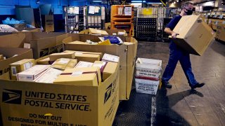 A worker carries a large parcel at the United States Postal Service sorting and processing facility