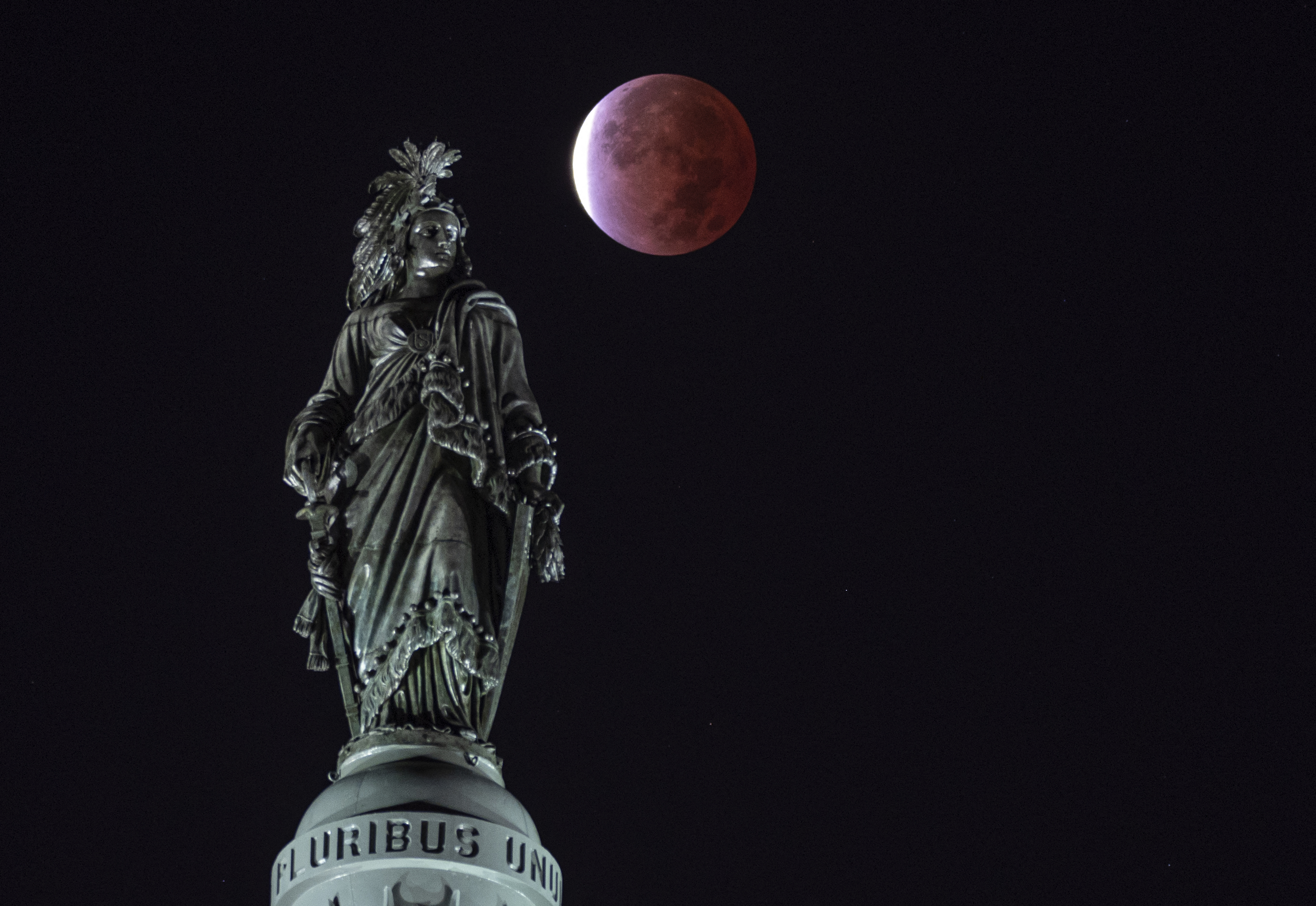 The moon, with a partial lunar eclipse, is seen behind the Statue of Freedom on Capitol Hill in Washington, D.C.