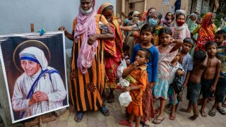 Homeless people gather beside a portrait of Saint Teresa