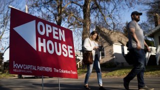 Dos potenciales compradores de vivienda pasando por delante de una casa en venta