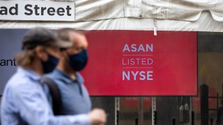 Pedestrians wearing protective masks pass in front of a banner displaying Asana Inc. signage during the company’s initial public offering (IPO) in front of the New York Stock Exchange (NYSE) in New York, U.S., on Wednesday, September 30, 2020.