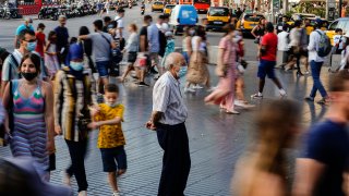 A man wearing a a face mask to protect against the spread of coronavirus pauses as people walk along a street in downtown Barcelona, Spain