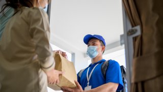 Male courier with bicycle delivers bag with food to the client's door.