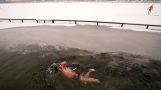 A man swims in the half-frozen water at the Shichahai Lake during a snow fall in Beijing, Sunday, Feb. 13, 2022. According to some of the local residents, swimming in the freezing water leads to health.