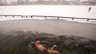 A man swims in the half-frozen water at the Shichahai Lake during a snow fall in Beijing, Sunday, Feb. 13, 2022. According to some of the local residents, swimming in the freezing water leads to health.