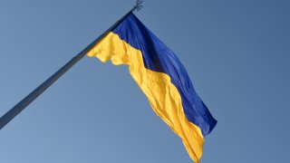 The flag of Ukraine on a pole in front of the sky. The top half of the flag is blue and the bottom yellow.
