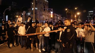 A crowd gathers to watch police working at the site where a a gunman opened fire in Bnei Brak, Israel, Tuesday, March 29, 2022. The circumstance of the deadly incident in the city east of Tel Aviv were not immediately clear.