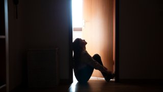 Backlit teenager sitting in a dark indoor doorway in contemplation