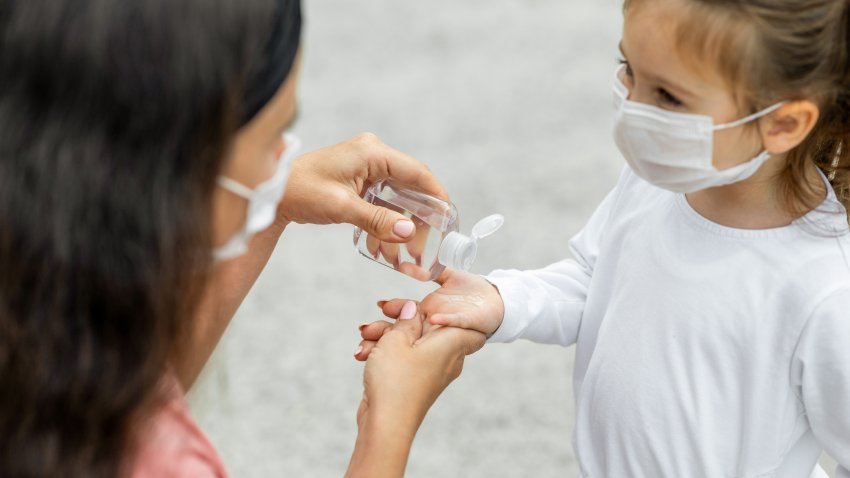 Mother and daughter disinfecting hands with sanitizer outdoors