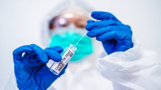 Doctor in protective gloves & workwear holding open test tube and taking out sampling swab for novel Covid-19 test