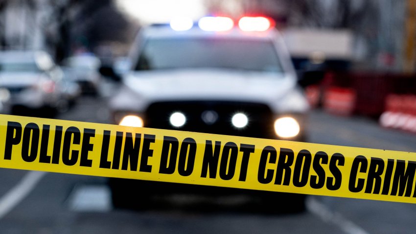 Police tape is seen in front of a police vehicle as Manuel Oliver displays a banner calling on government officials to prioritize gun violence prevention from a construction crane near the White House in Washington, DC, on February 14, 2022. – Olivers son Joaquin Oliver was killed in the Parkland School shooting four years ago today. (Photo by Stefani Reynolds / AFP) (Photo by STEFANI REYNOLDS/AFP via Getty Images)