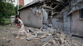 A girl carries a dog as she walks past a house damaged from shelling in the Leninsky district of Donetsk, on the territory which is under the Government of the Donetsk People's Republic control, eastern Ukraine, Monday, June 6, 2022.