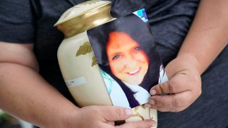 Kelly Titchenell sits on her porch in Mather, Pa., holding a photo of her mother Diania Kronk, and an urn containing her mother's ashes, July 7, 2022.