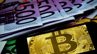 The bitcoin logo displayed on a smartphone with euro banknotes in the backgrouund.