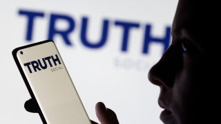 The Truth social network logo is seen displayed behind a woman holding a smartphone in this picture illustration taken February 21, 2022.