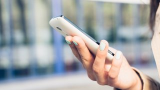 A hand holding a white mobile phone.