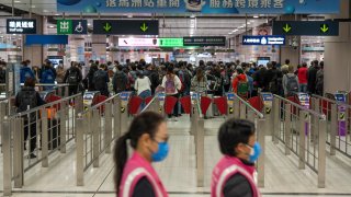 Workers wearing face masks walk by as travelers wait at the departure hall of the Lok Ma Chau station following the reopening of crossing border with mainland China